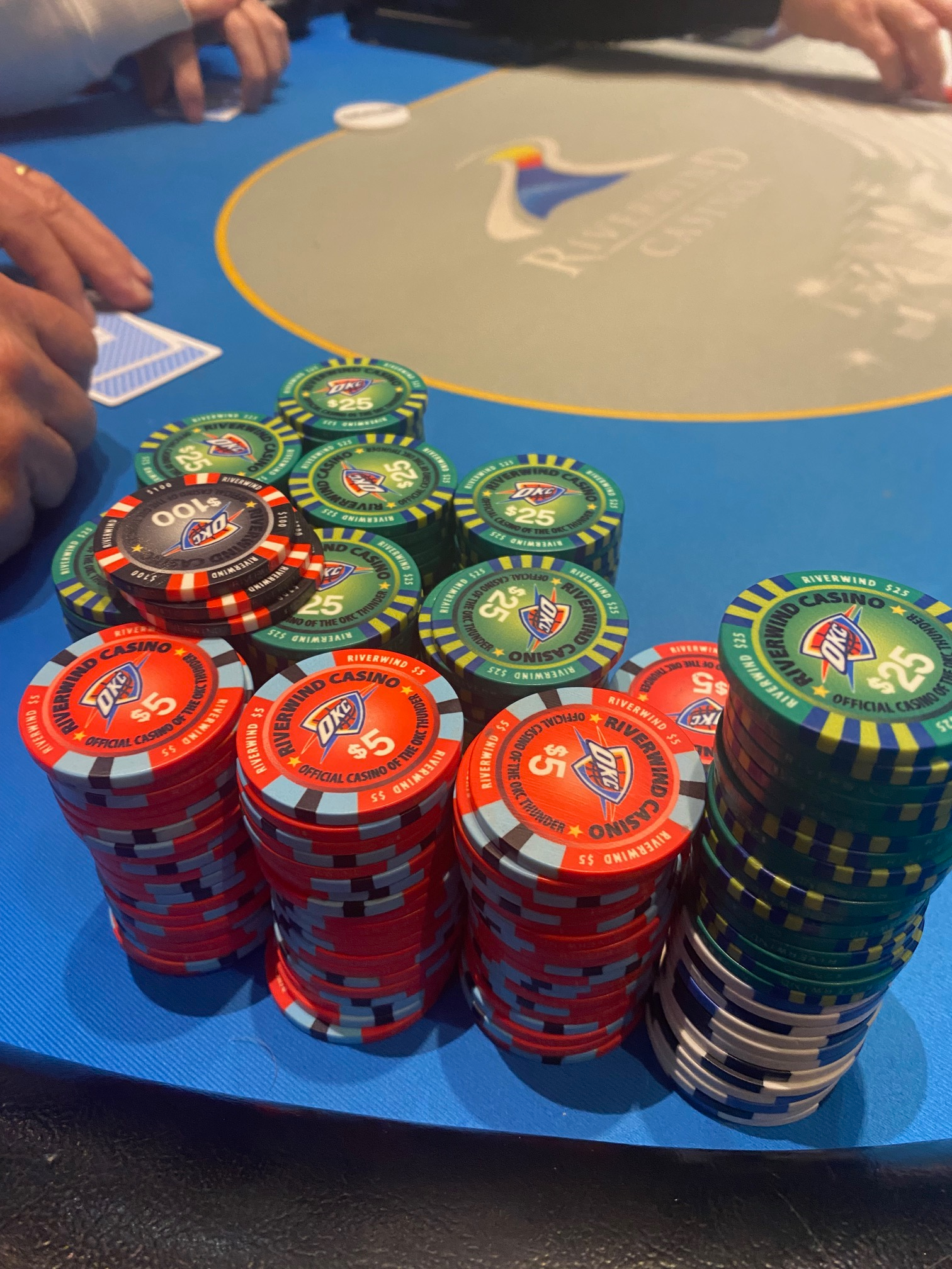 Colorful red, green, black, and white casino chip stacks on blue Riverwind Casino felt